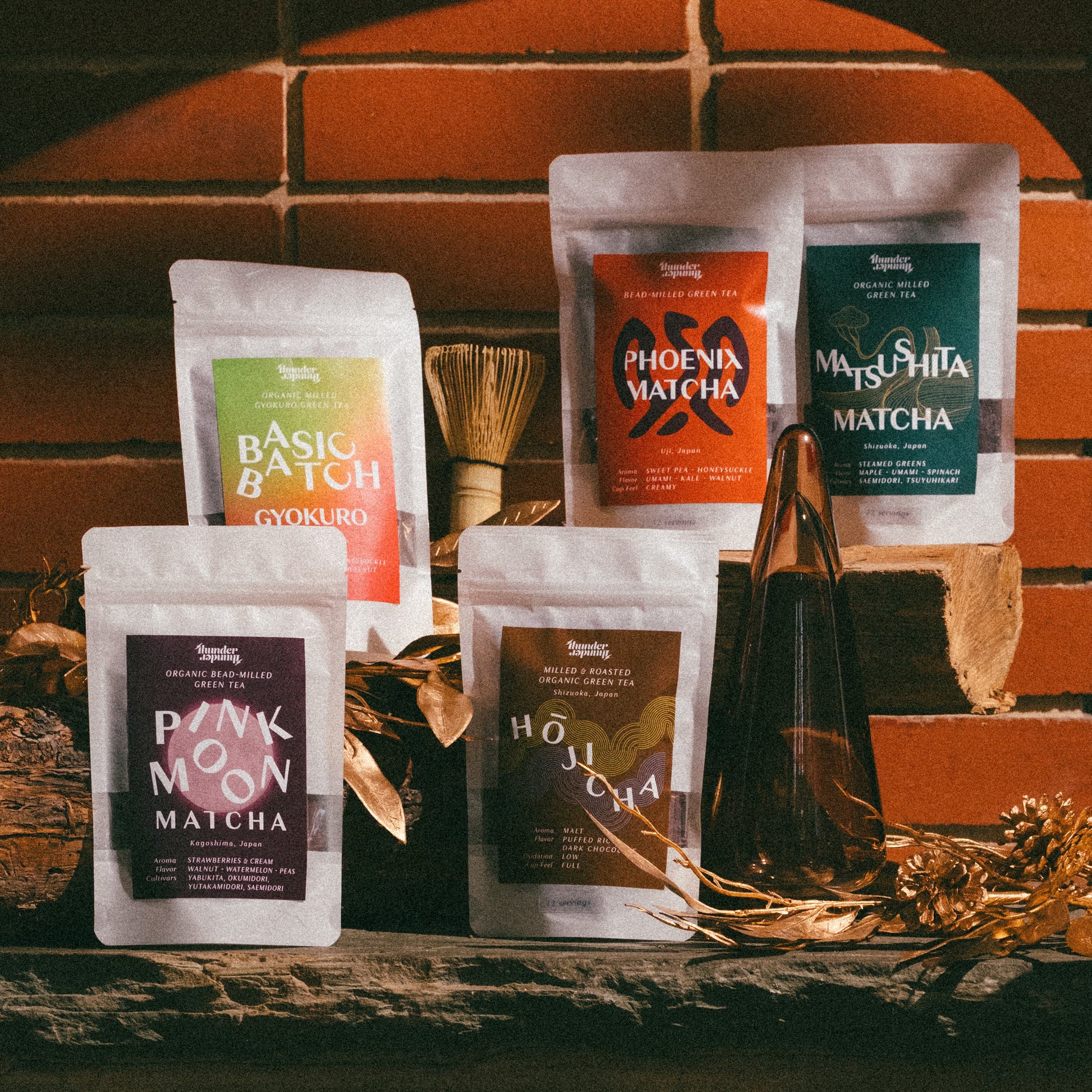 Collection of matcha, hojicha, gyokuro milled tea packages on a wooden surface with a warm-toned tile background.